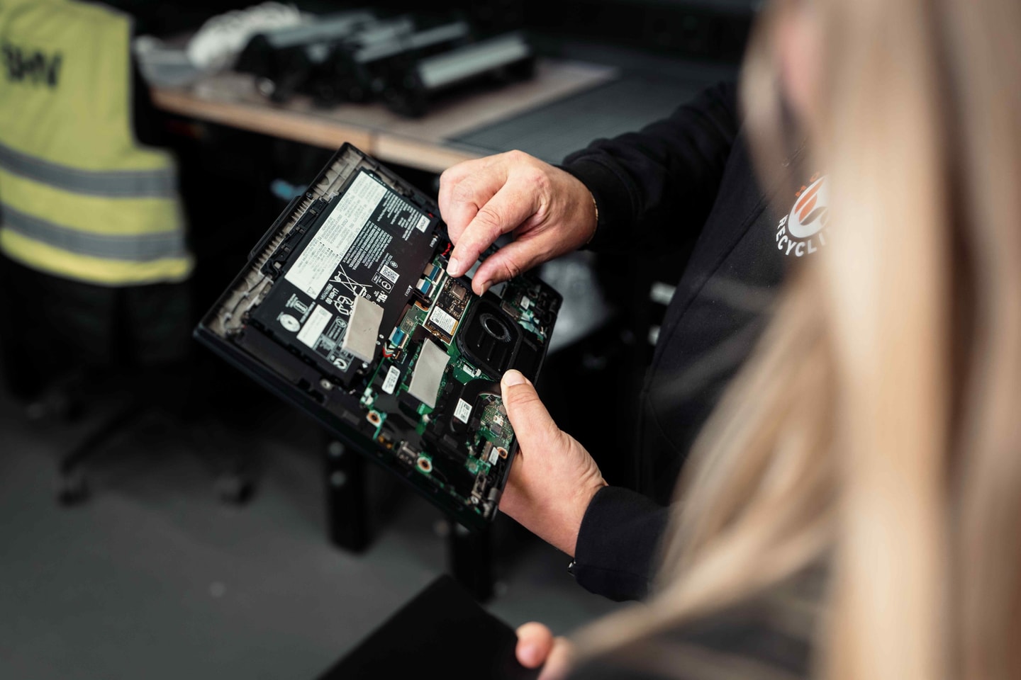 Twee handen houden een opengewerkte laptop vast met de printplaat zichtbaar