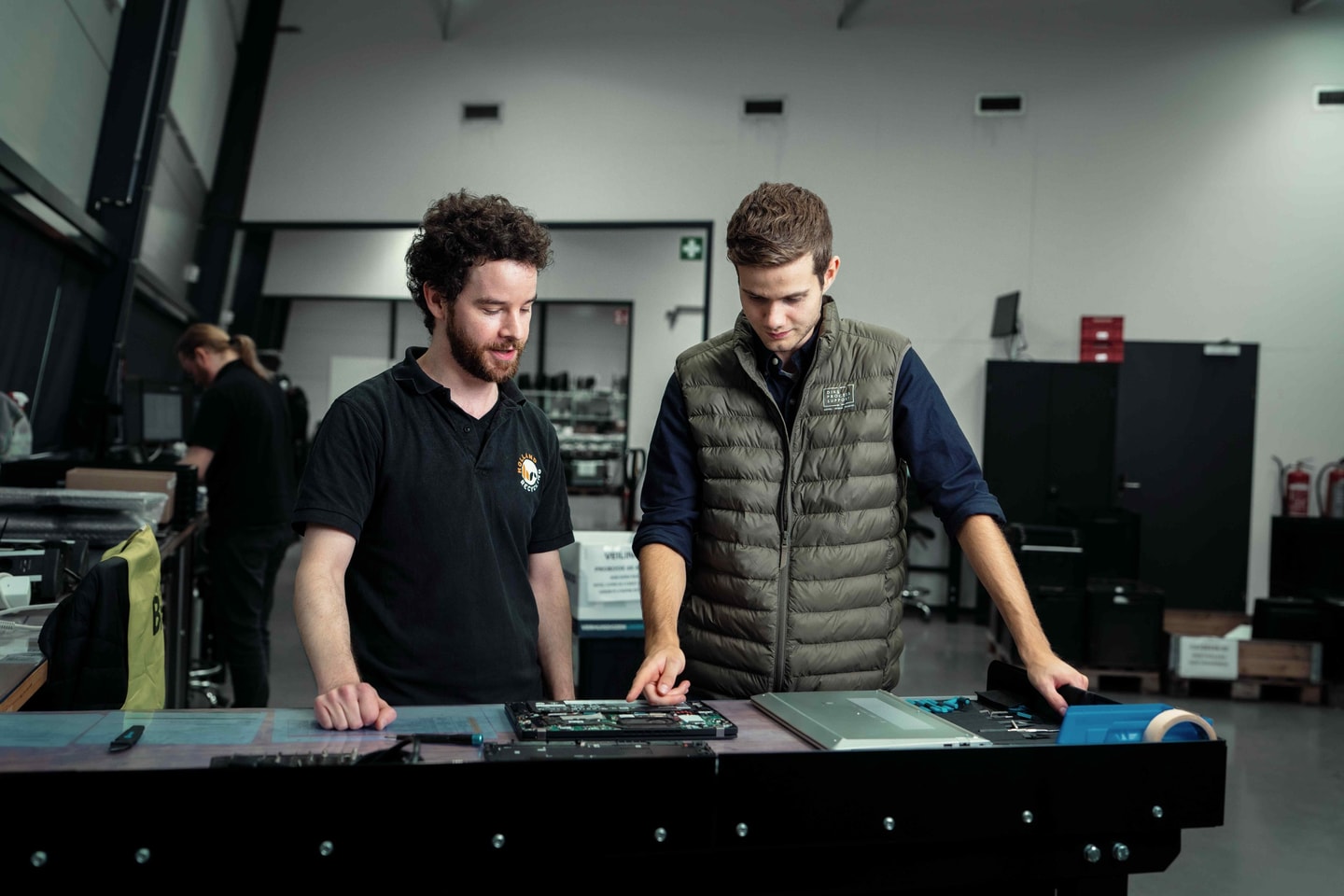 Twee mannen buigen zich over apparatuur op een werkbank in een technische ruimte