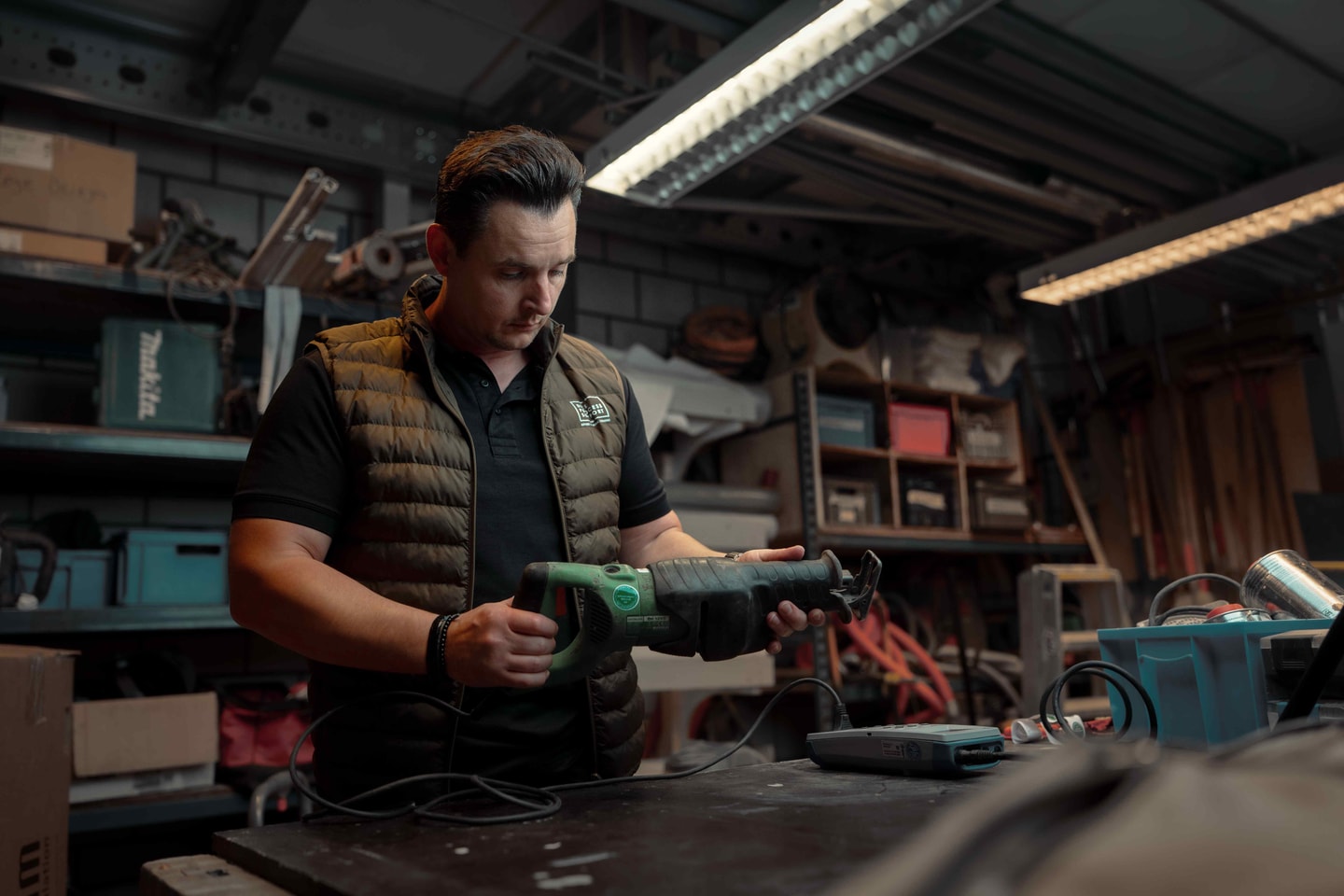 Man in bodywarmer test een elektrisch gereedschap aan een werkbank