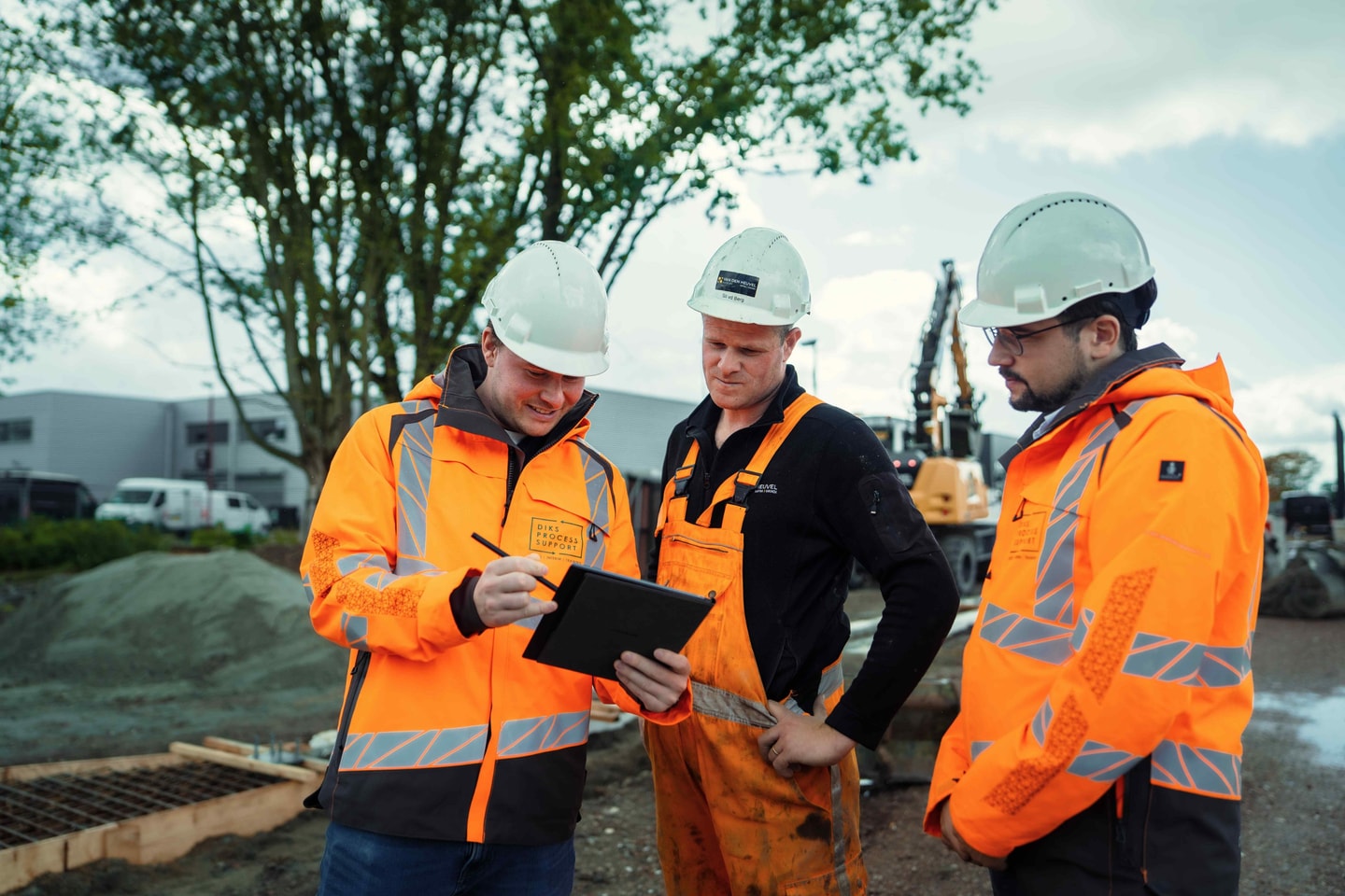 Drie mannen met witte helm bekijken samen een tablet op een bouwplaats