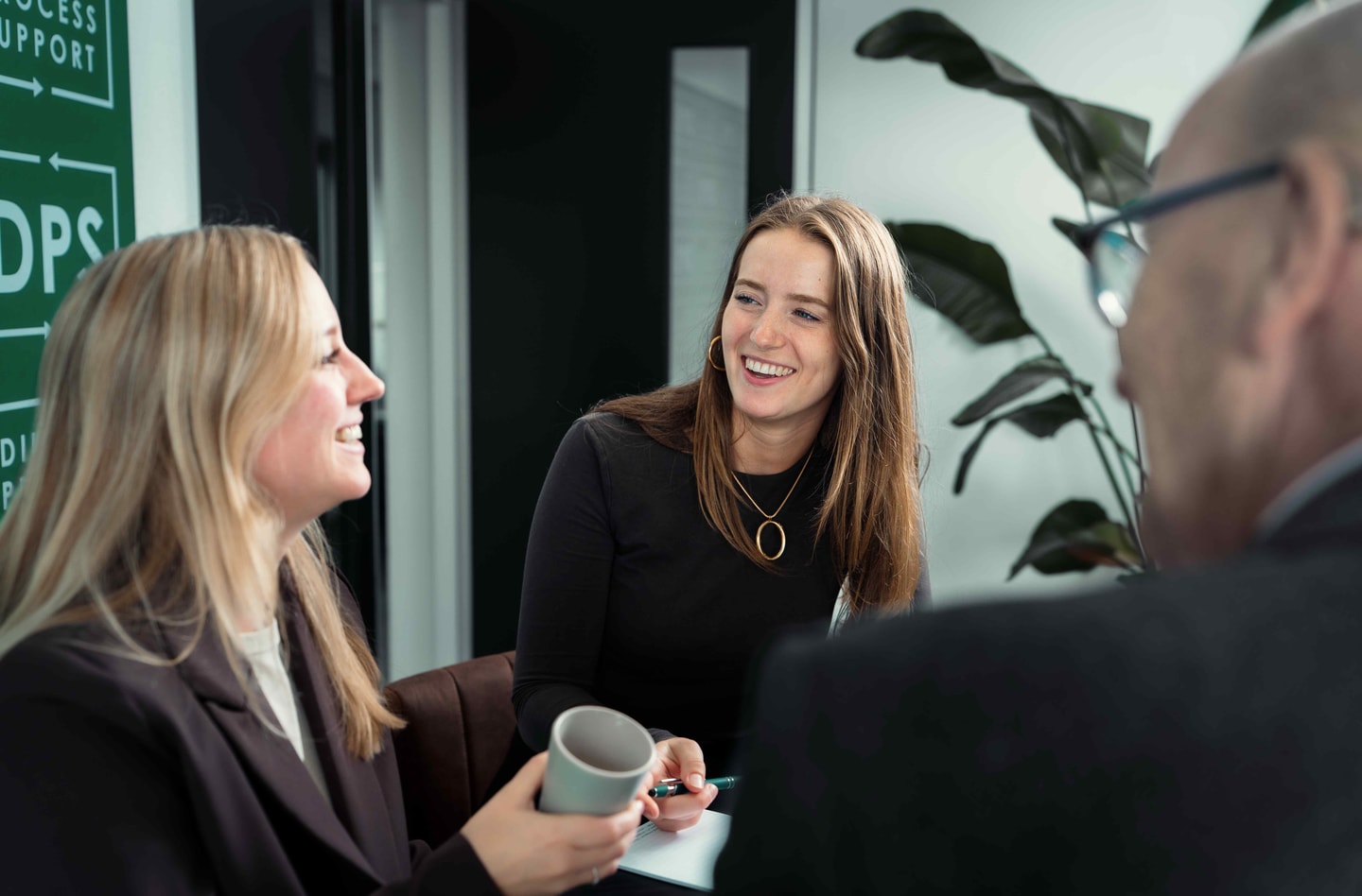 Drie mensen in gesprek met koffie in een kantoor met planten
