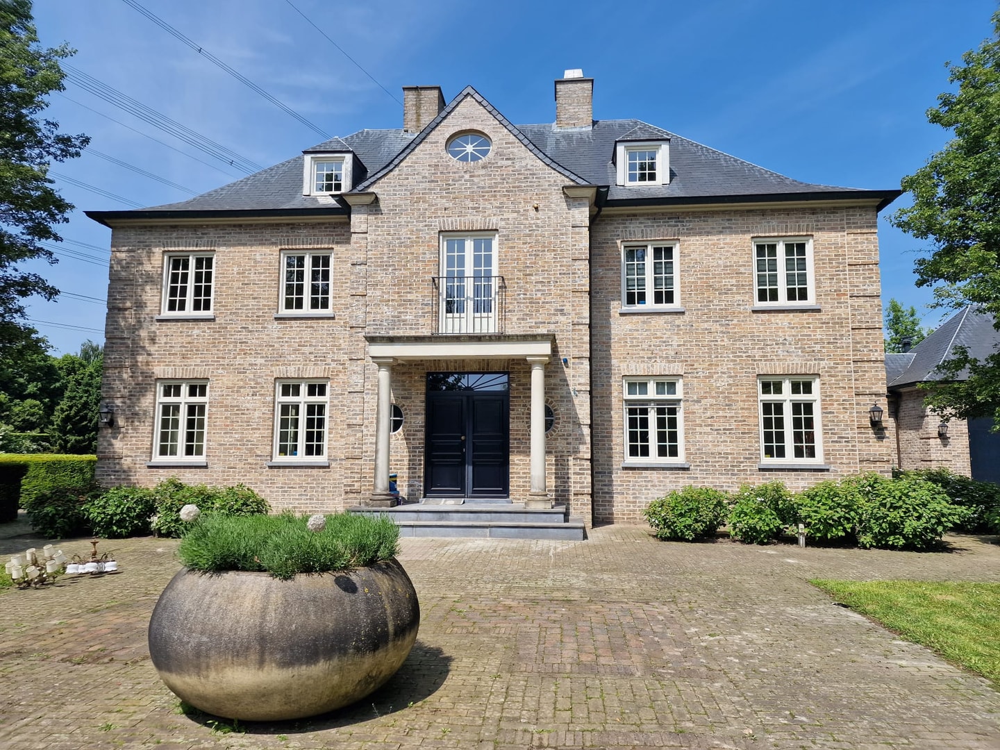 Statig bakstenen kantoorpand met een grote plantenbak voor de deur