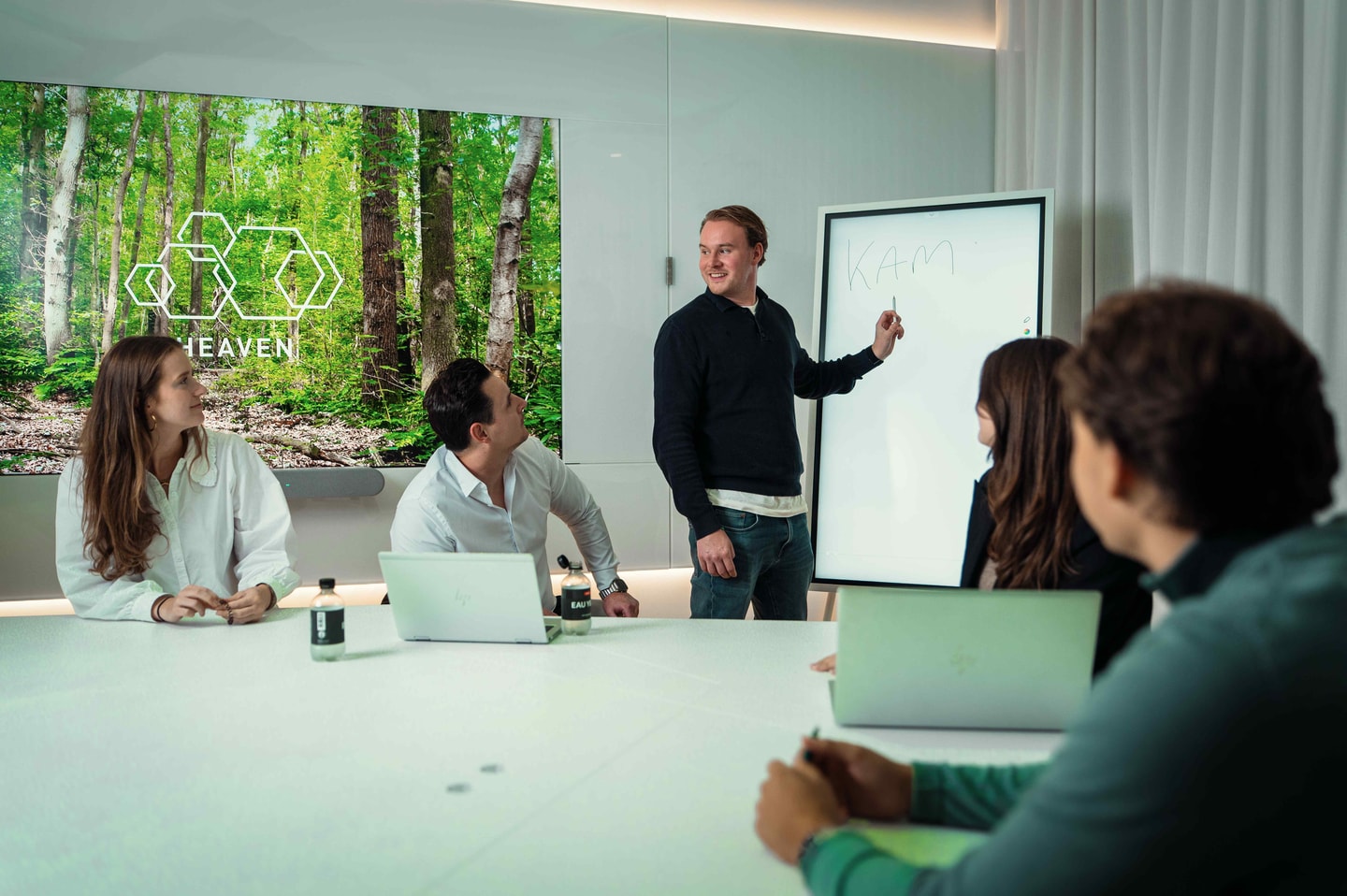 Man geeft uitleg bij een whiteboard aan collega’s met laptops